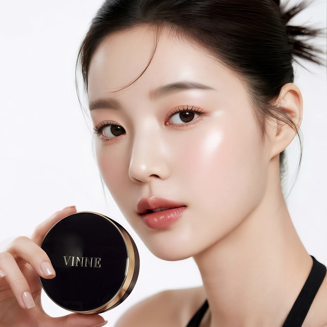 A detailed close-up portrait of a model with luminous 'Glass Skin' finish, holding a black and gold Vinne Cushion Foundation compact. 