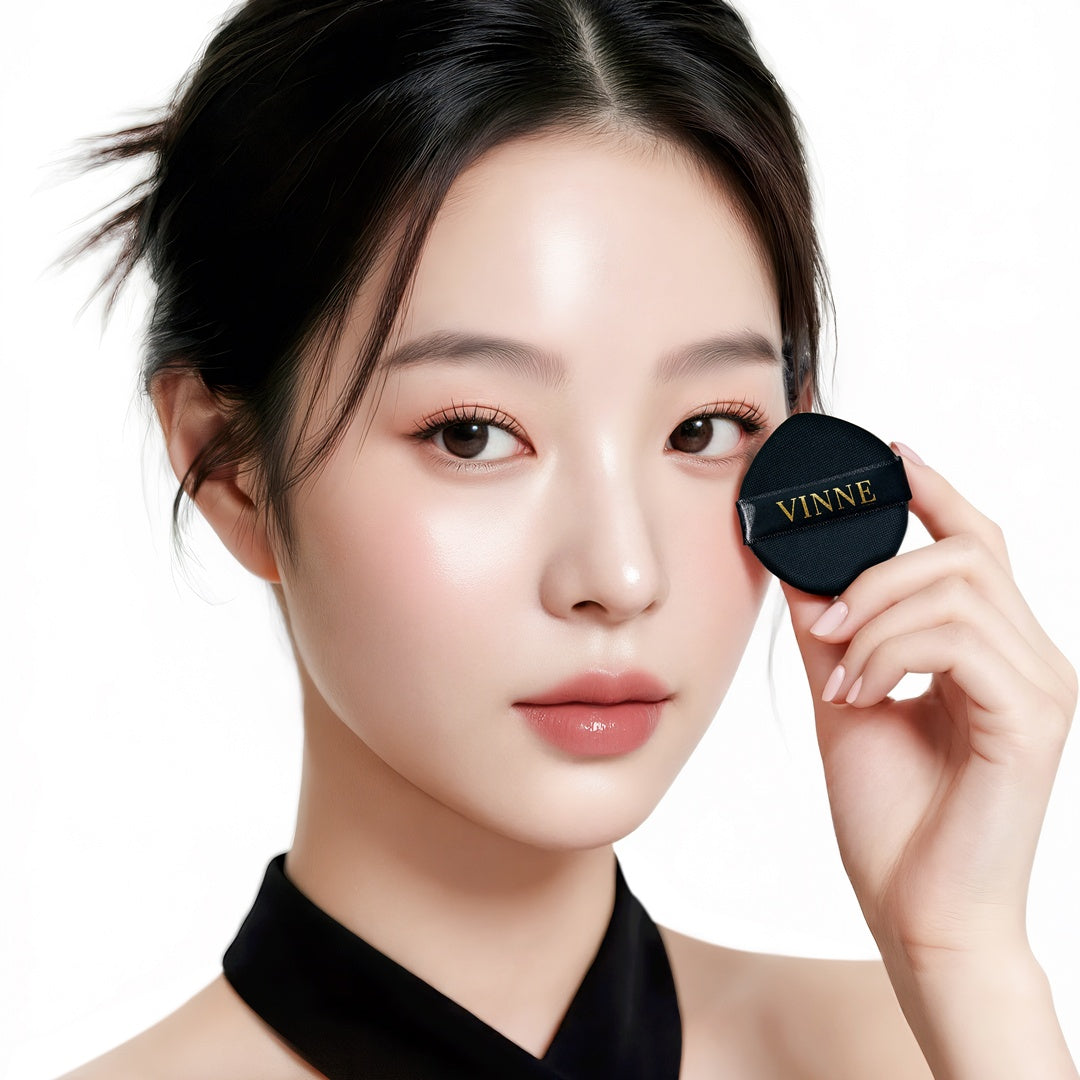 A beauty model showcasing a radiant glass skin finish while holding the VINNE luxury black and gold cushion compact.